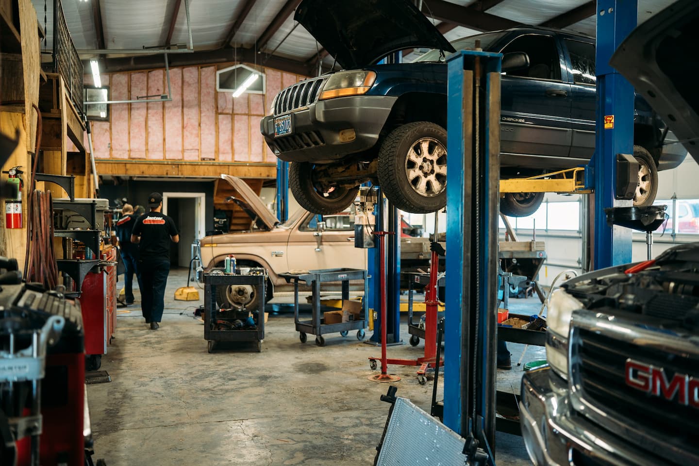 Inside the shop: a Jeep up on a lift, a Ford truck with its hood open, and a technician walking between the bays